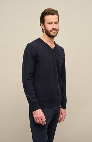 Ein männliches Model trägt den Kaschmirpullover „Nio2.0-WS“ von Frauenschuh in der Farbe Midnight (Dunkelblau); das luxuriöse, weiche Kaschmirmaterial verleiht dem Hoodie eine edle Haptik und optimale Wärme für Herbst und Winter; der Pullover hat einen feinen Rippenstrick an Saum und Ärmelabschlüssen